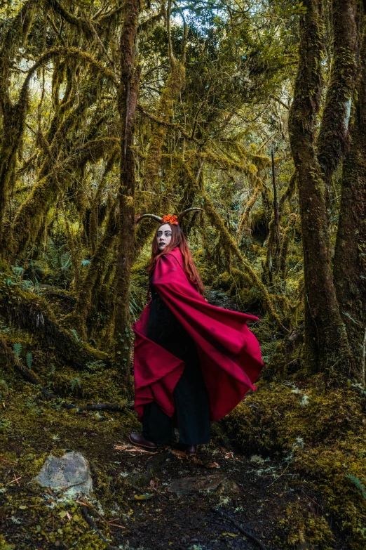 a woman dressed as a red queen walking through the forest