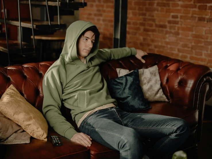 a man sitting on a leather couch wearing a hoodie