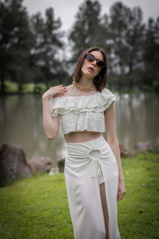 the woman is wearing a white skirt while posing in front of a lake