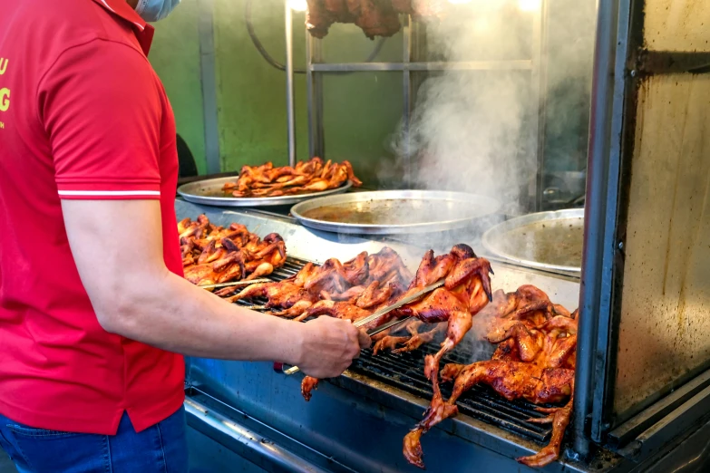 a man in red shirt preparing chicken on top of grill