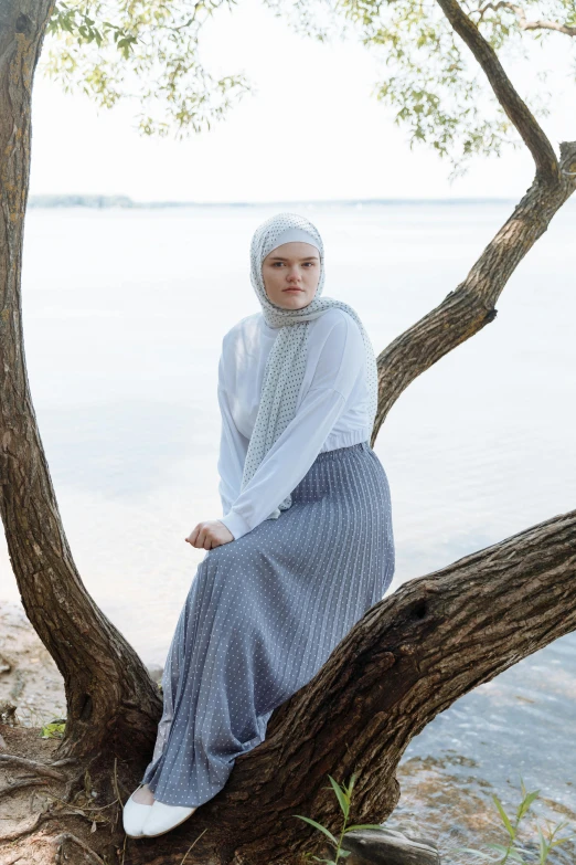 a woman is sitting in a tree near the water