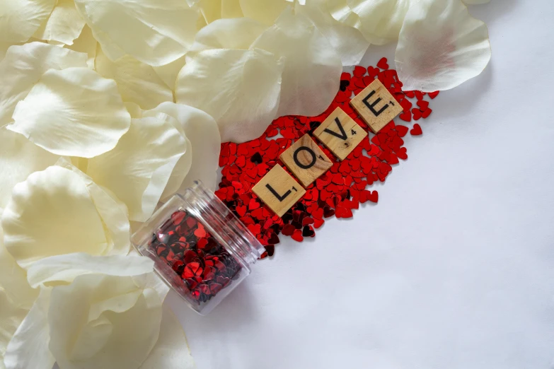 a red glittered bottle with the word love sits on a bed of petals