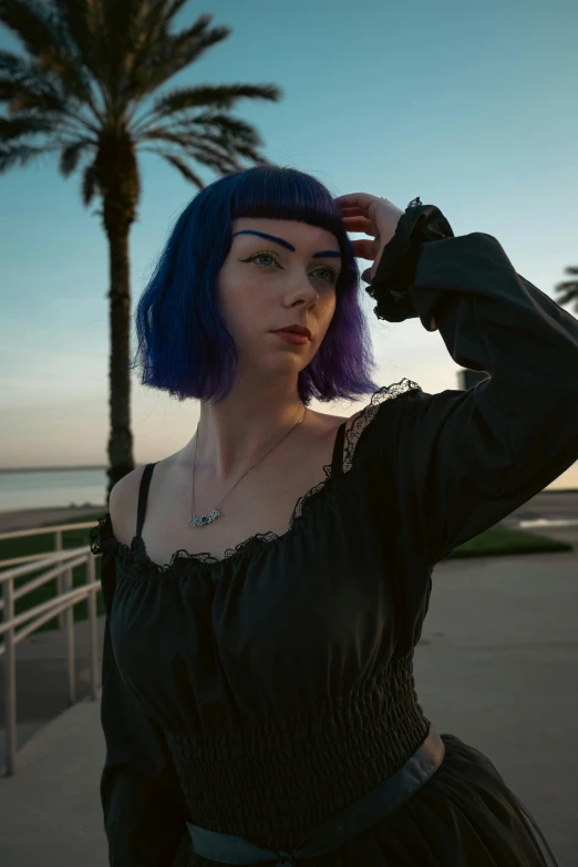 a woman with blue hair is standing near a palm tree