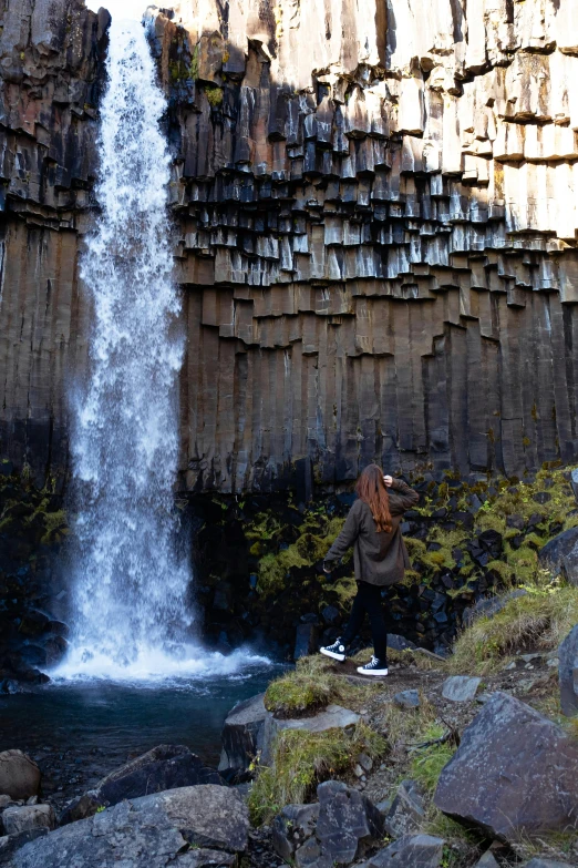 a woman is taking pictures at the bottom of a waterfall