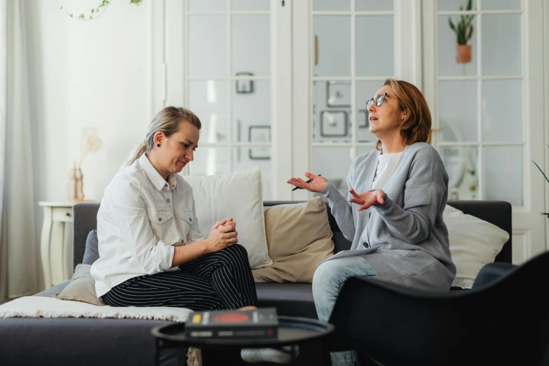 two women sitting on the couch in front of a window