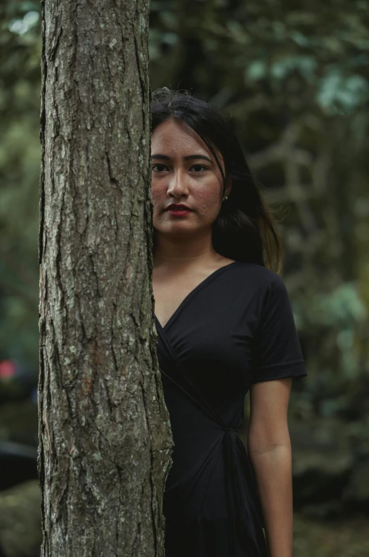 a girl in a black dress standing between a tree