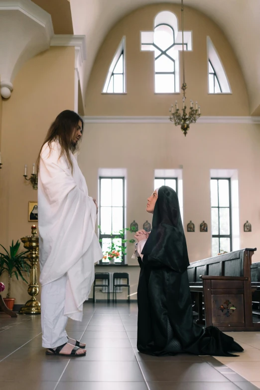 the image shows a priest and a nun in the room with large windows