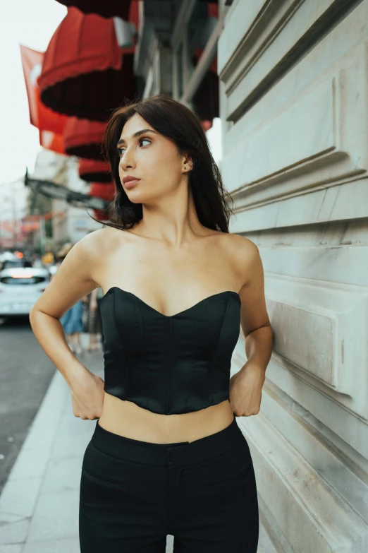 woman posing in black outfit, standing outdoors by building