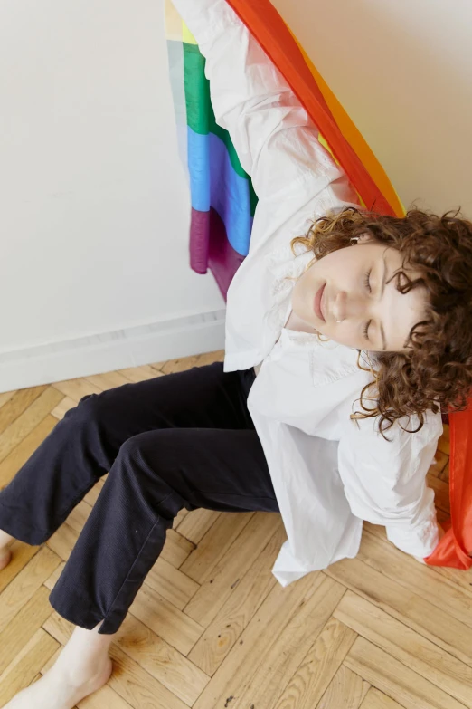 a woman lies down with her head turned to the right while her hand is in her pocket and rainbow streamers hang above her