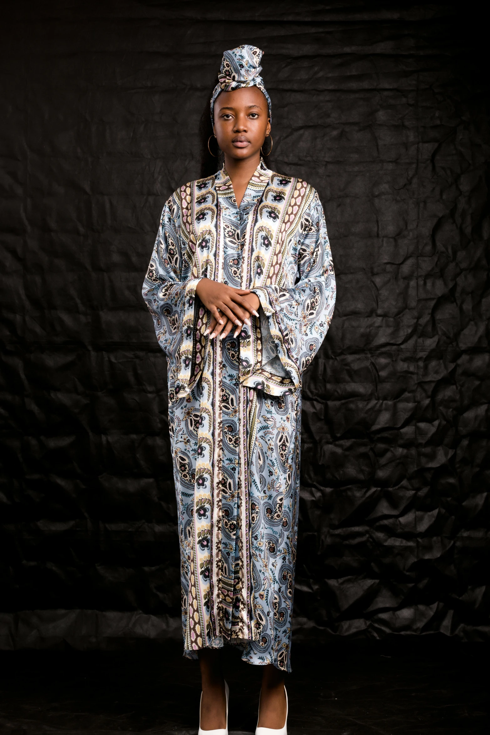 a woman standing on a black floor wearing an african robe