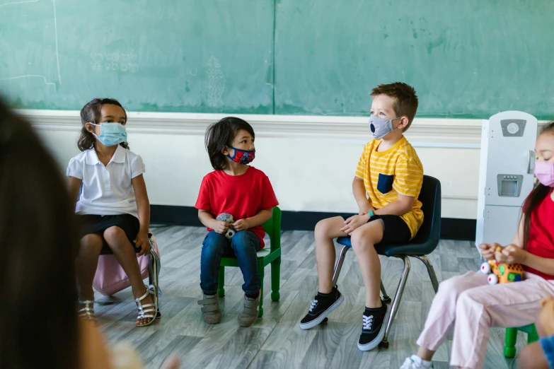 some children sitting in chairs wearing masks