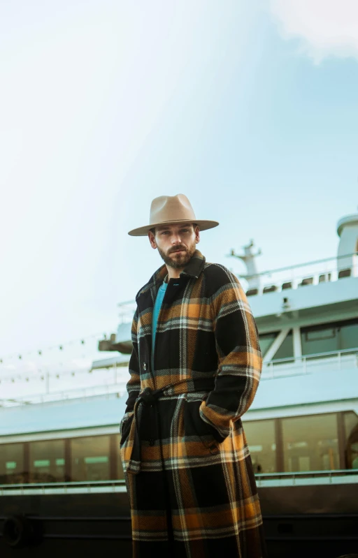 a man wearing a hat and coat stands near train