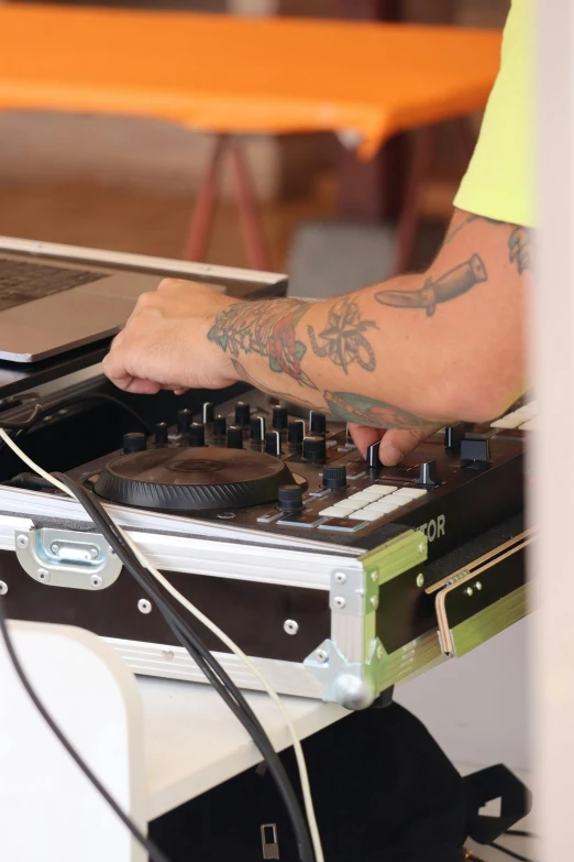 man with arm tattooed using a dj's deck in front of a laptop
