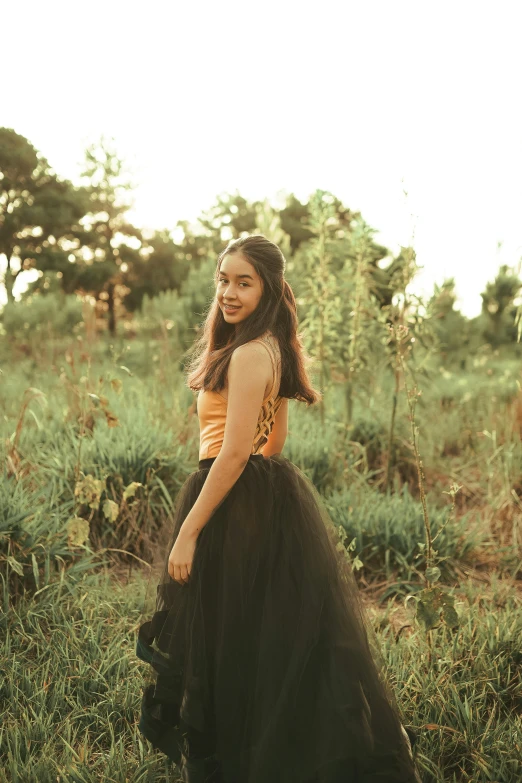 girl in dress poses for camera outdoors near trees