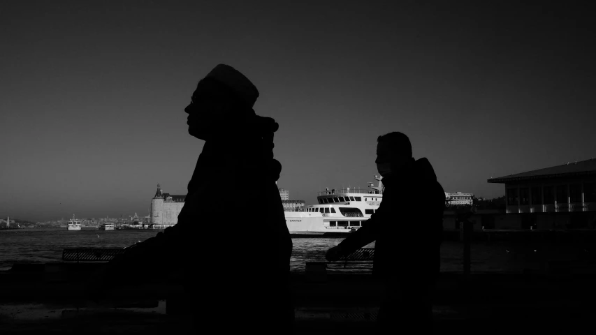 two people walking in silhouette across a bridge near a boat