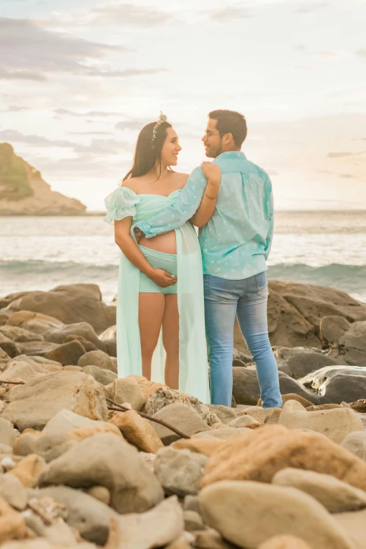 a pregnant couple on the beach in front of a cloudy sky