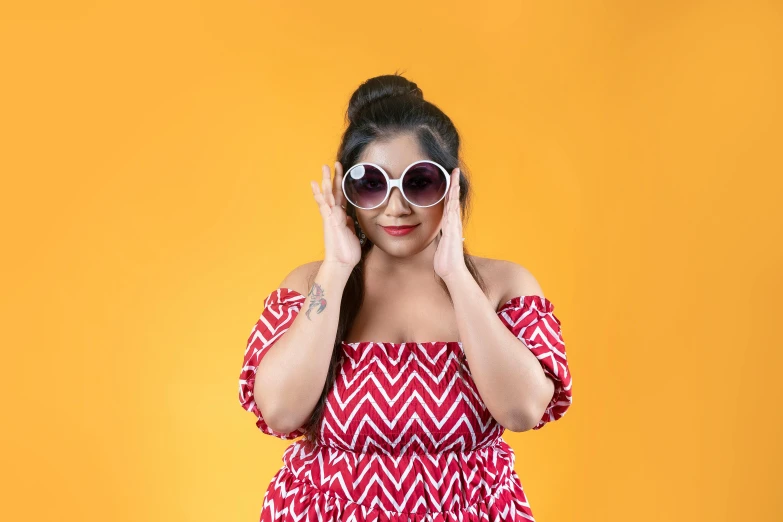 the woman wears sunglasses as she poses against a yellow background