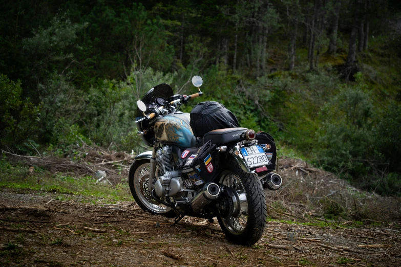 a motorcycle parked on a dirt road next to a lush green forest