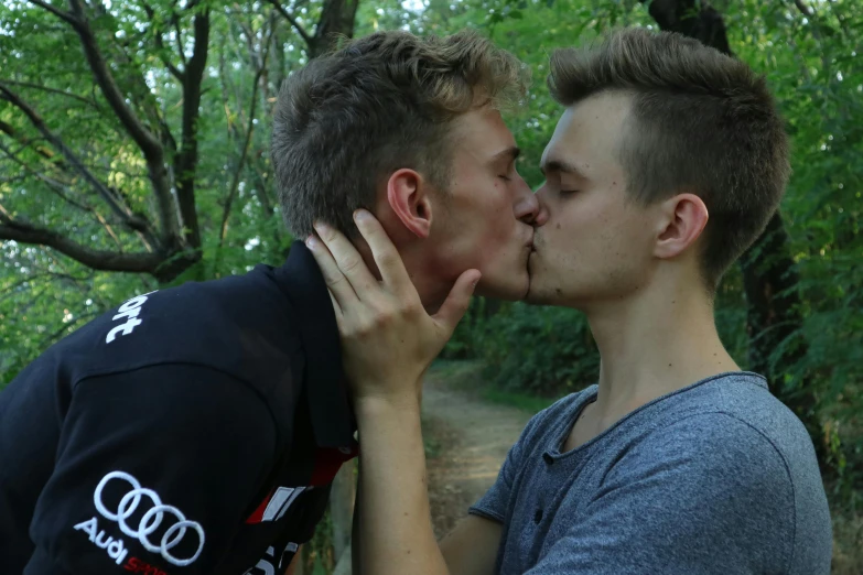 two young people kiss each other while standing in front of some trees