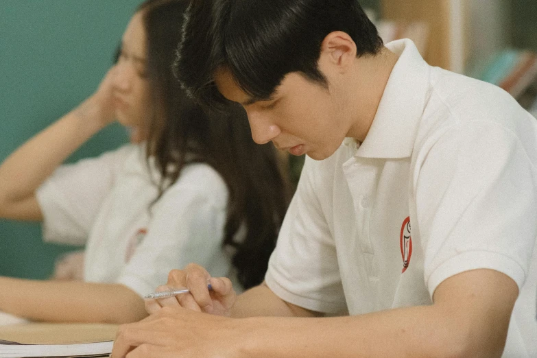 a man writes at a table while two other people watch