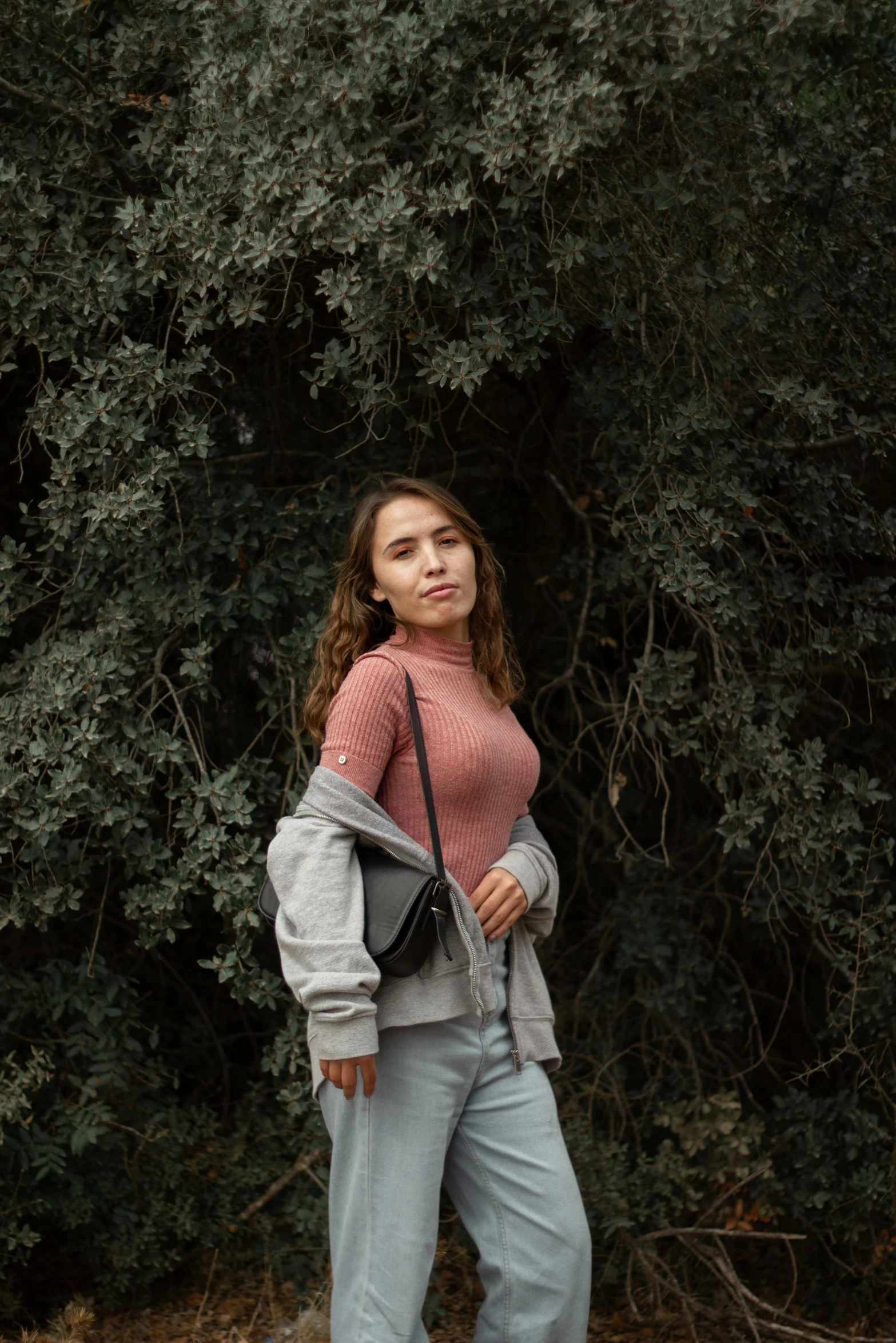 young woman in pink shirt, blue pants and brown shoeless boots standing on street corner