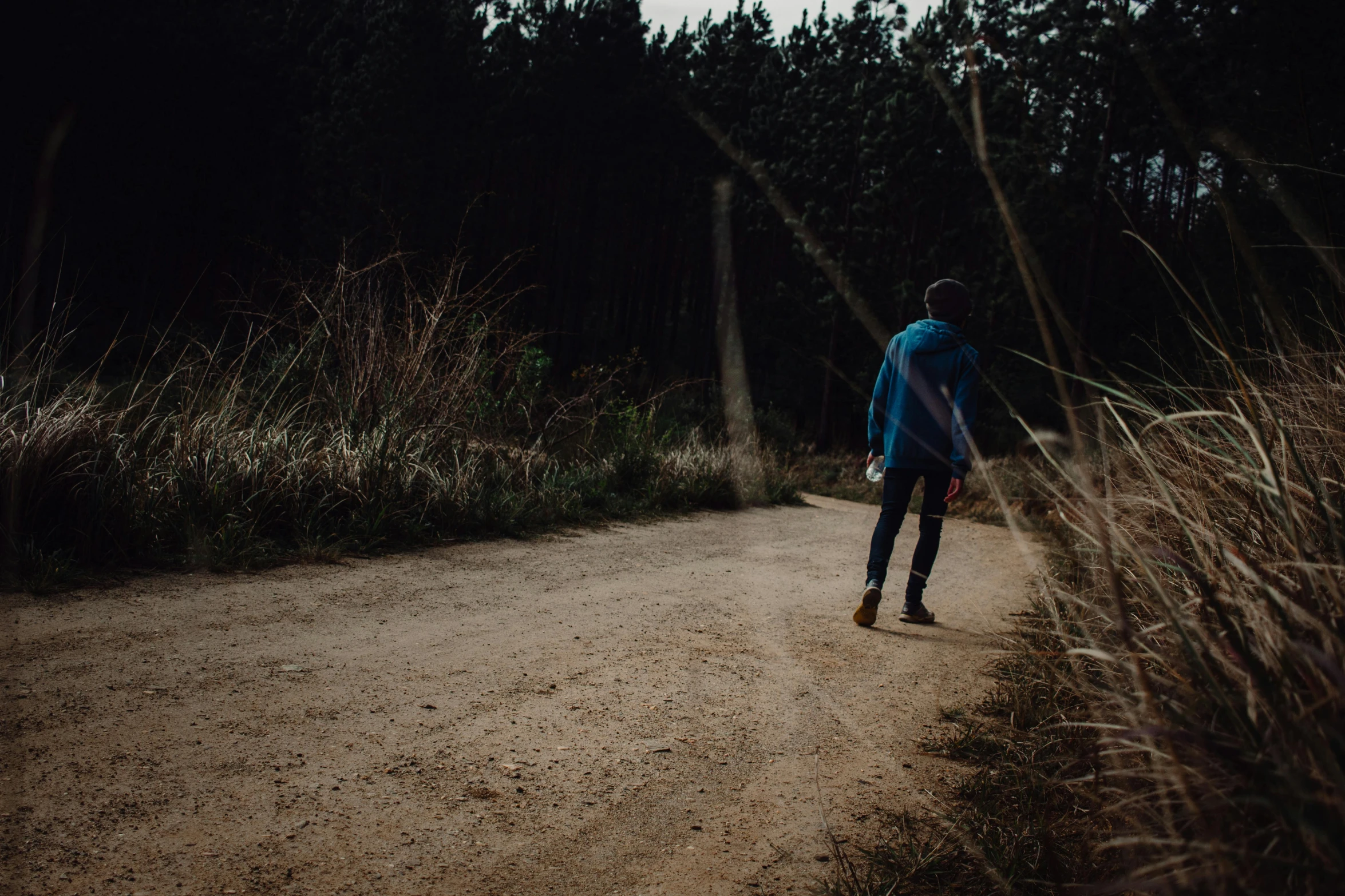 a man walking down a dirt road past grass