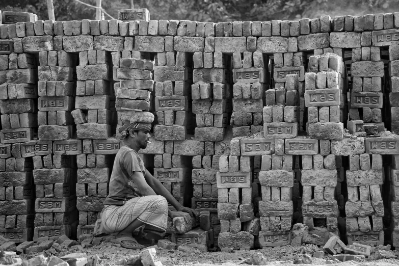 a man sitting next to a huge stack of bricks