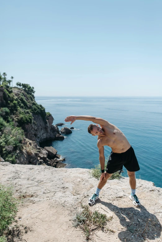 a man standing on a cliff above the ocean throwing a frisbee