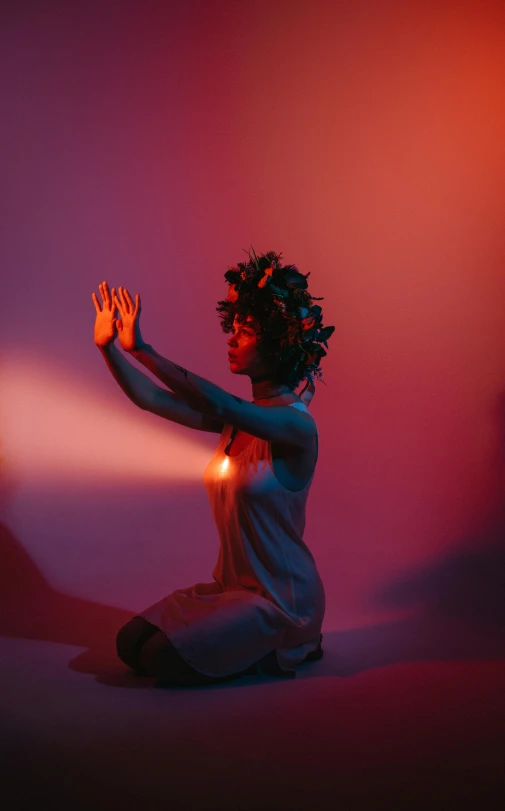 a woman sits cross legged in the dark holding her hand