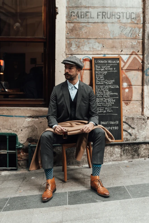 a man sitting down wearing a hat and holding a coat