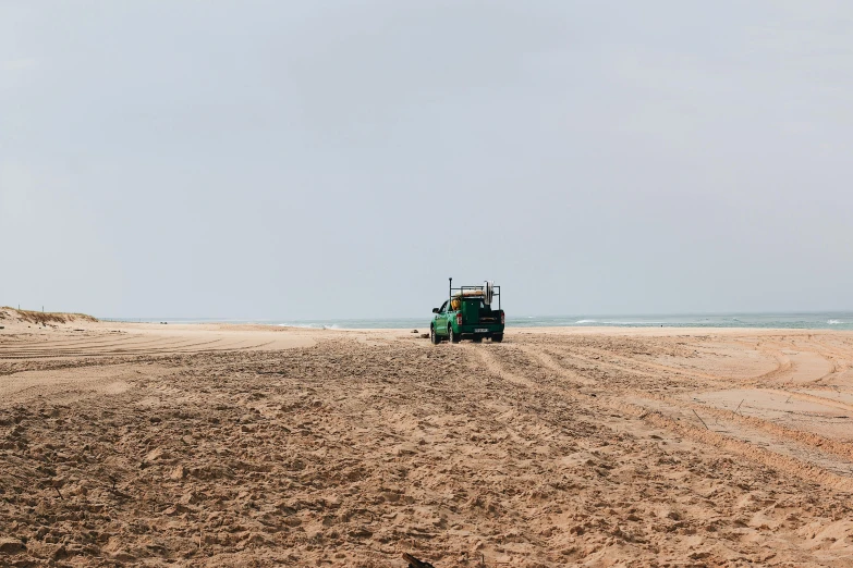 a green tractor driving on the beach near the ocean