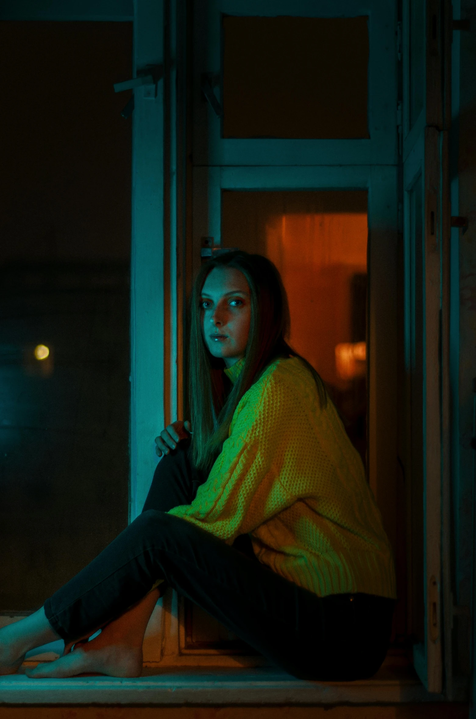 a woman sitting on a windowsill in the dark