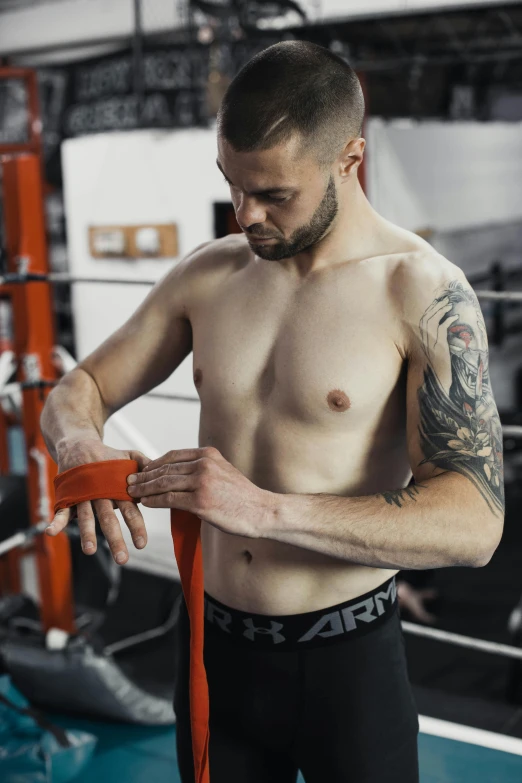 shirtless man with a tattooed arm and chest holding a pair of gloves