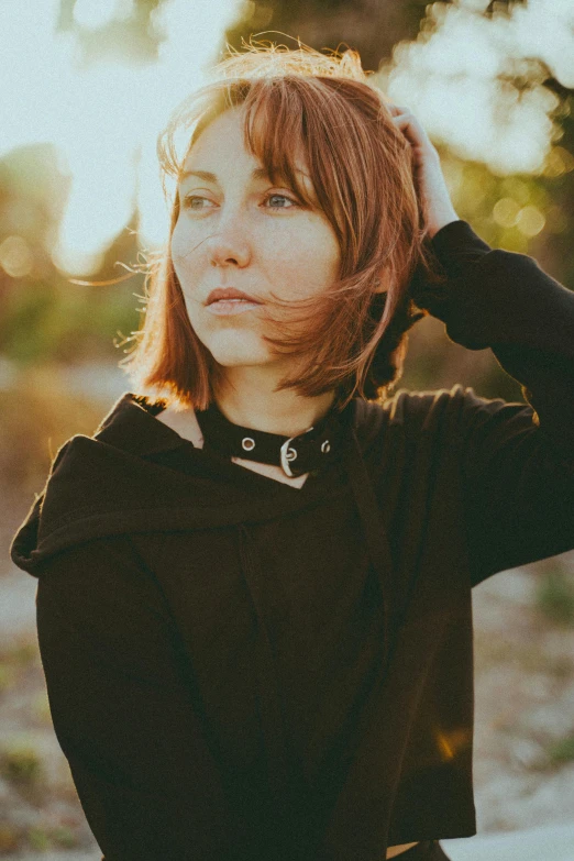 the girl is wearing a sweater and leaning against the tree