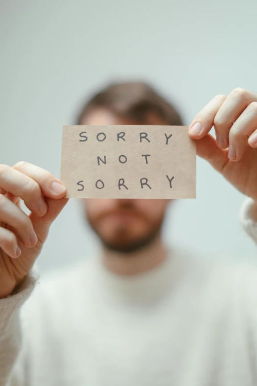 a man holding a piece of paper that reads sorry not sorry