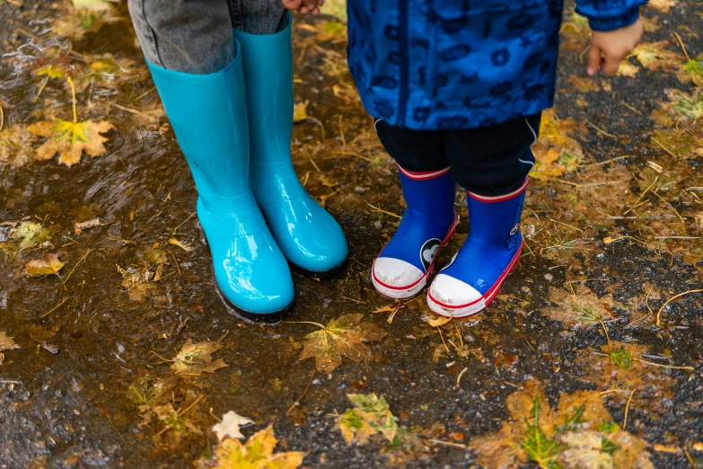 two people wearing blue rain boots standing in the mud