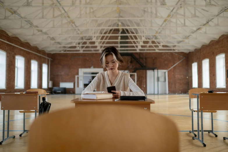 a female student sits in a chair and looks at a phone while studying