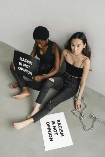 two young women sitting on the ground with signs