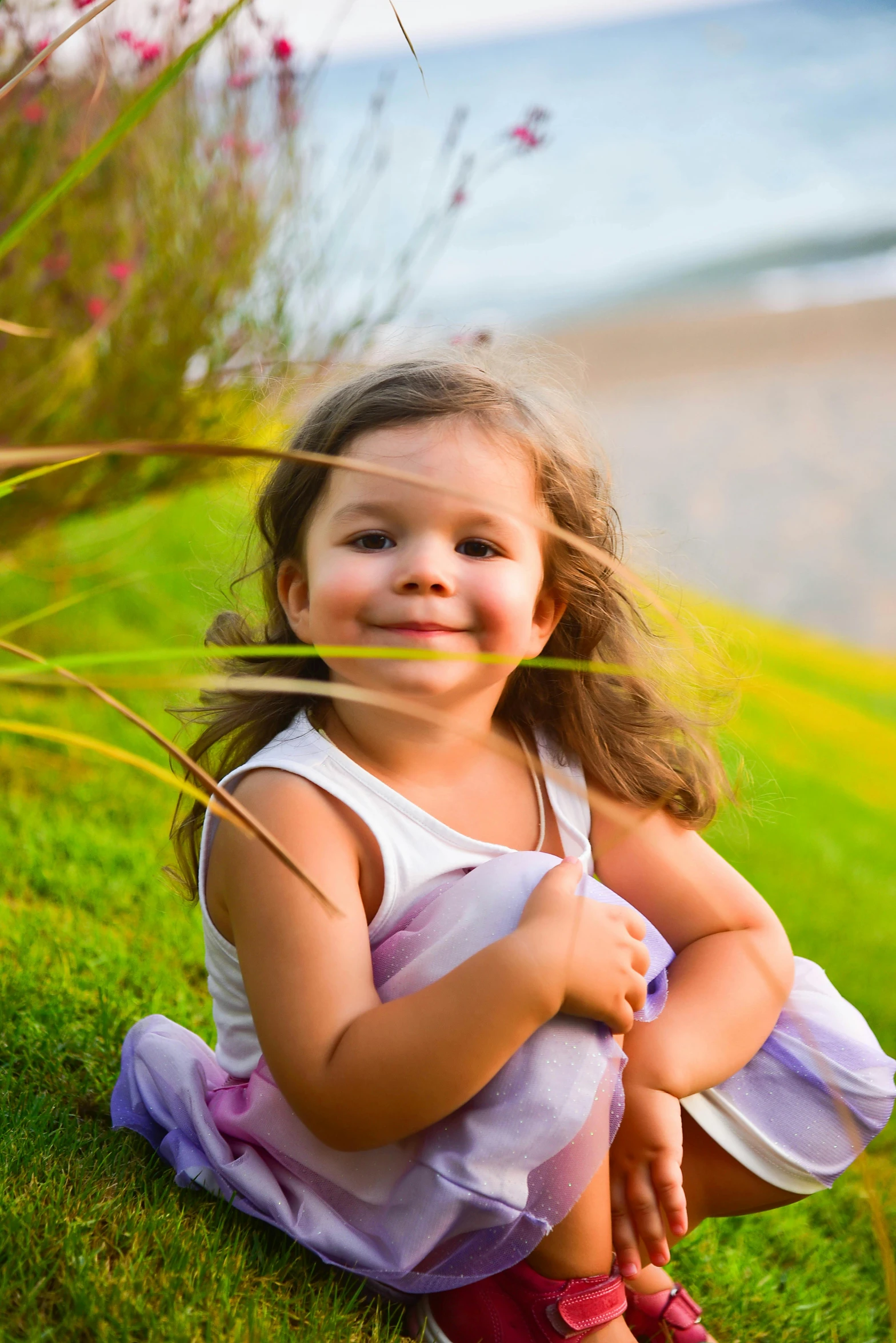 an adorable little girl with long brown hair sitting on the grass