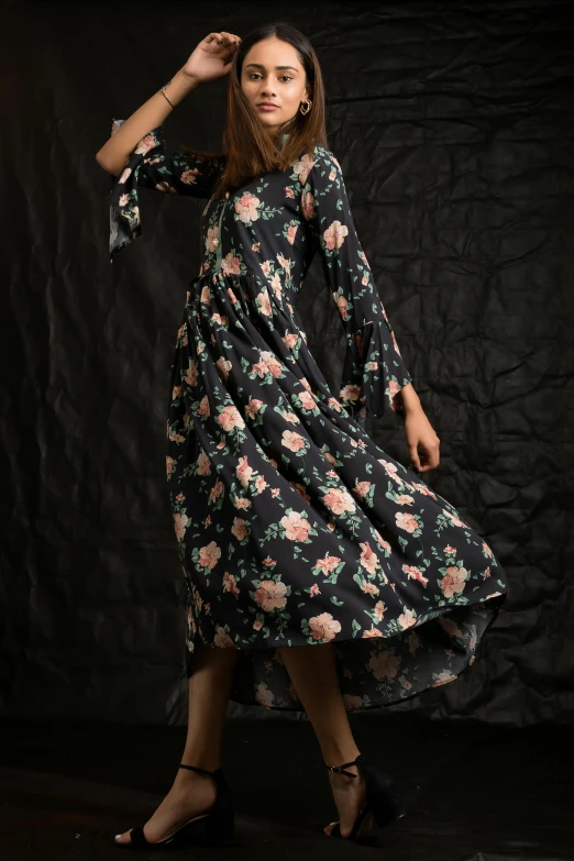 a woman standing with her hand on her hip wearing a flowery print dress