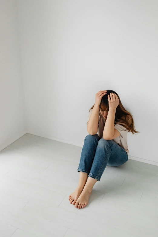 the woman is seated against a white wall with her head on her hands