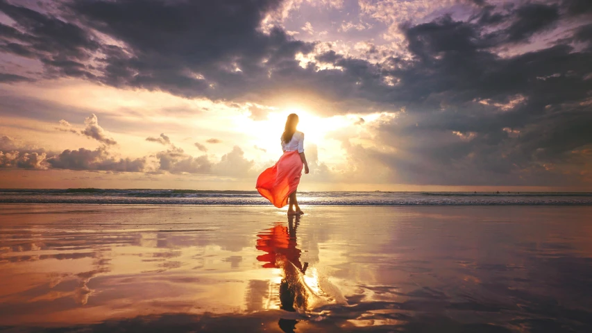 the young woman in red dress is walking on the beach at sunset