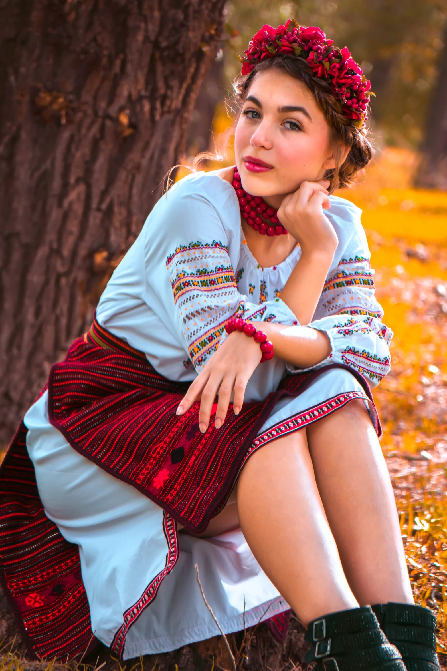 a woman sitting in front of a tree in a dress and scarf