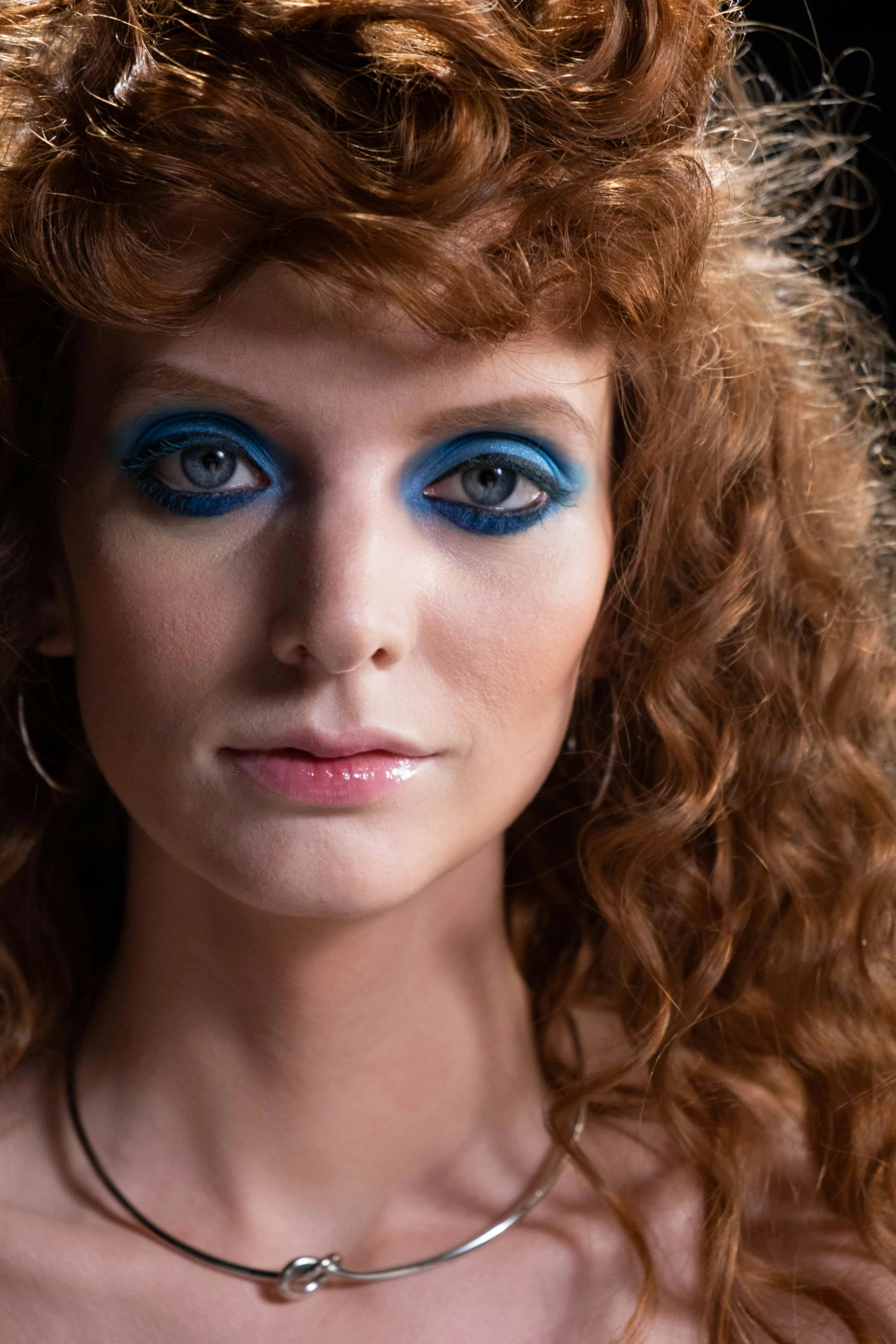 a woman with red curly hair wearing blue makeup and big eyes