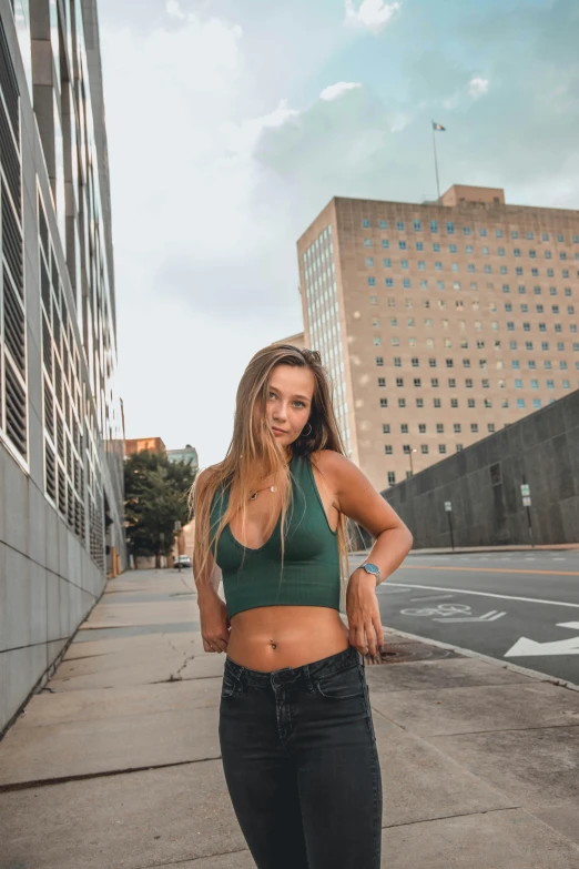 a woman in black jeans and a green crop top standing outside on a street