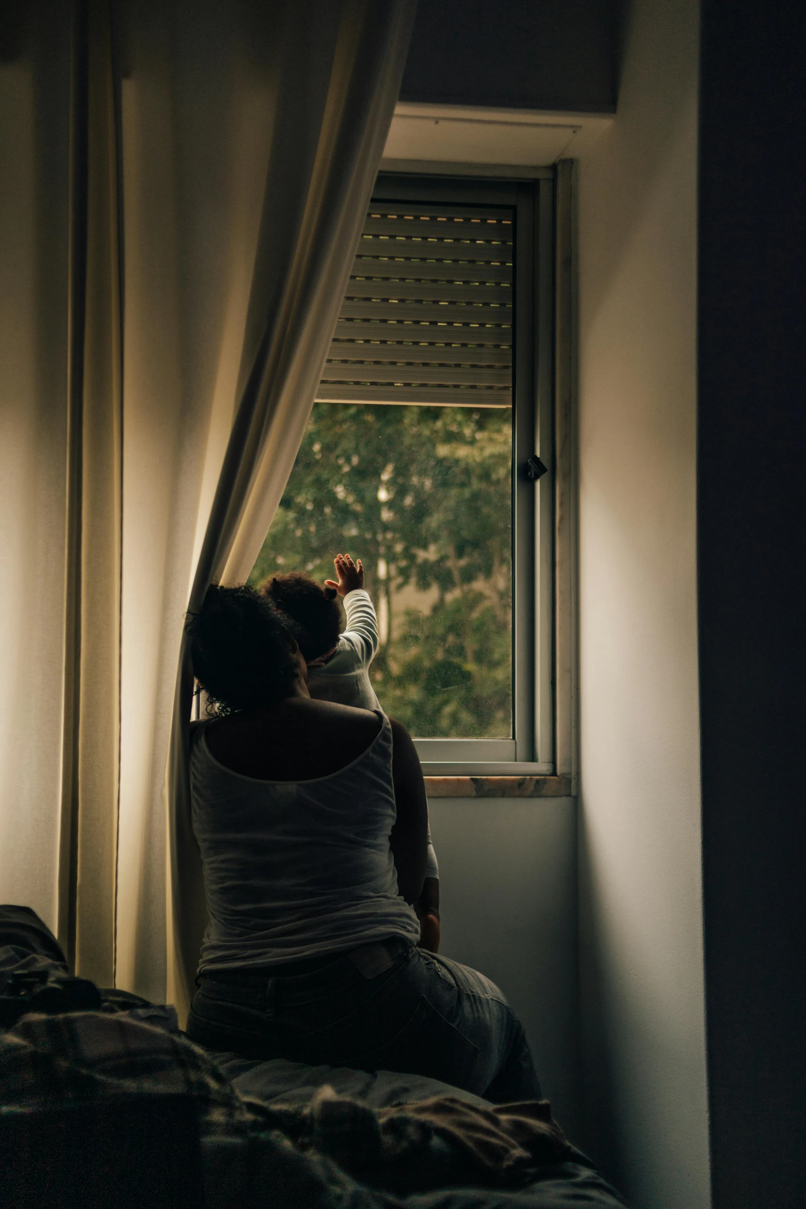 a woman is sitting on the bed staring out of a window