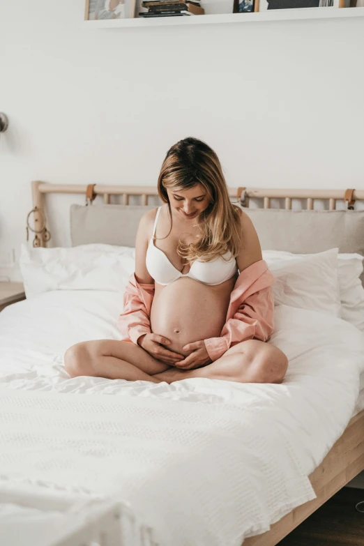 a pregnant woman is sitting on her bed looking down