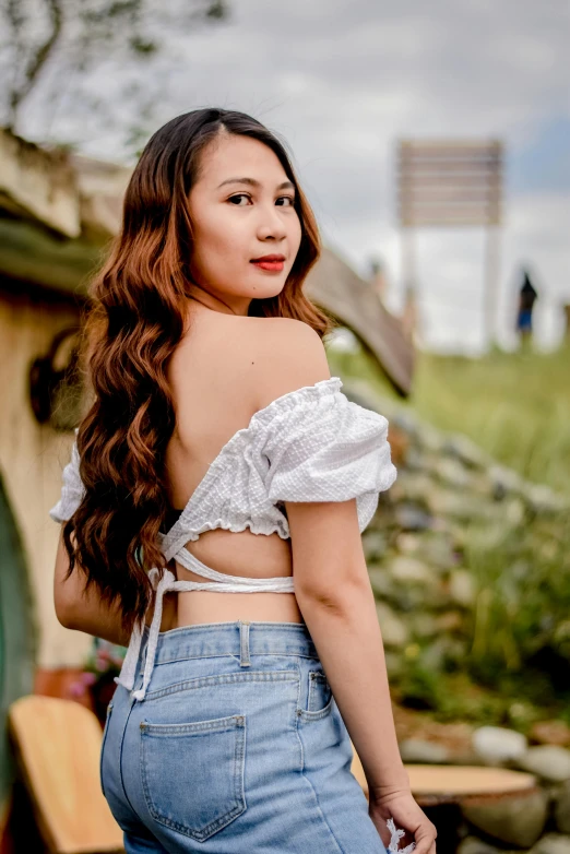 a woman wearing jeans standing in front of a shack