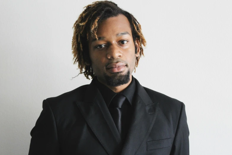 a black man with dreadlocks wearing a dark suit and dark tie