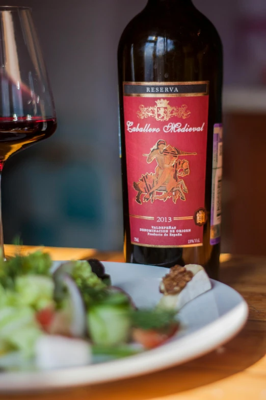 a close up of a plate of food with salad and a bottle of wine